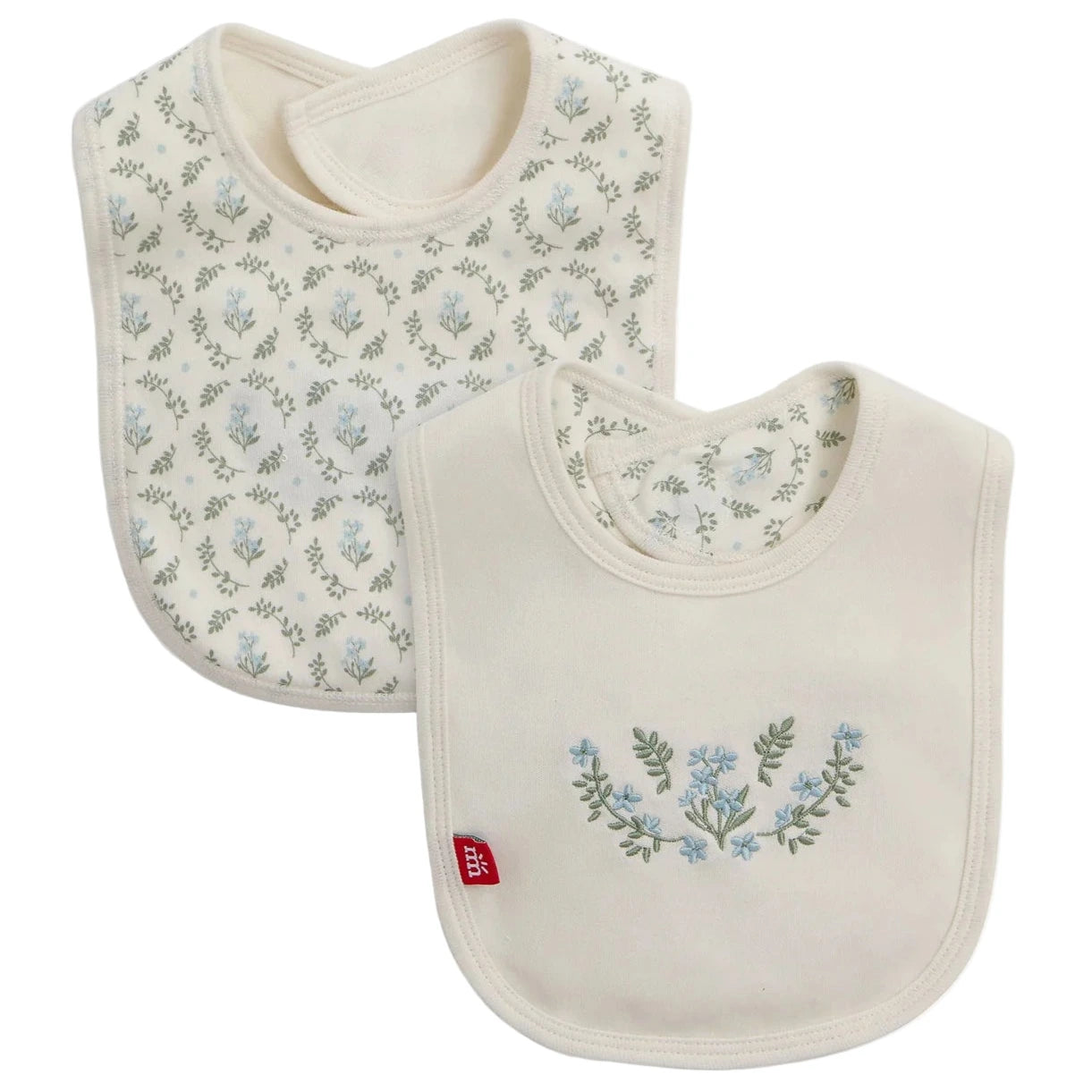 The Magnetic Me Eloise Organic Cotton Reversible Bib with Emb features two GOTS-certified bibs in cream with blue floral patterns: one with an all-over print, the other with a central floral design and a small red side label.