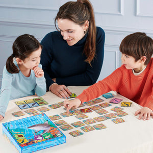 An adult and two children sit at a table playing Eeboo’s Sharks & Friends Shiny Memory Matching Game, an educational activity featuring colorful cards.
