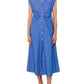 A woman stands against a white background wearing the Callas Milano Miami Dress—a sleeveless, collared, blue stretch chambray midi shirt dress—paired with flip-flops.