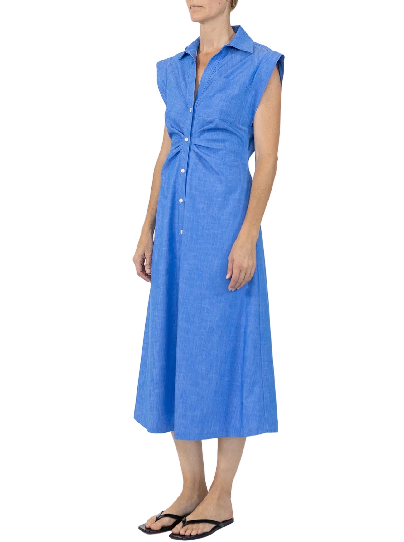A person wearing the Callas Milano Miami Dress, a sleeveless blue midi shirt dress with a collar, paired with black flip-flops, stands against a white background.