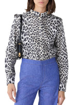 A person wearing the Callas Milano Mika Top in black and white cheetah print, tucked into high-waisted blue pants, paired with a black shoulder bag.