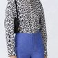 A woman wears the Callas Milano Mika Top in black and white cheetah print with long sleeves, tucked into high-waisted blue pants, and carries a black shoulder bag.