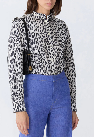 A woman wears the Callas Milano Mika Top in black and white cheetah print with long sleeves, tucked into high-waisted blue pants, and carries a black shoulder bag.
