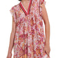 A person wearing the Poupette St Barth Sasha Mini Dress exudes true beach style—this short dress features a floral pattern with shades of pink, red, and orange, complemented by a V-neckline and ruffled sleeves. The creation from Poupette St Barth is adorned with intricate detailing around the neckline and hem.