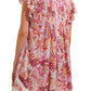 A person wearing the Poupette St Barth Sasha Mini Dress from the back, showcasing its short length and vibrant floral pattern in shades of pink, red, and orange. The beach-style dress is adorned with ruffled sleeves and a pleated upper back design.