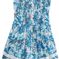 The Poupette St Barth Girls' Sasha Mini Dress is a sleeveless white dress that features blue floral patterns, ruffled shoulders, pleated detailing, and charming embroidery accents.