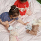Two young children sit on a striped blanket, using a Konges Slojd Blue Dot Tea Party Set to host a pretend play session for their two stuffed animals.