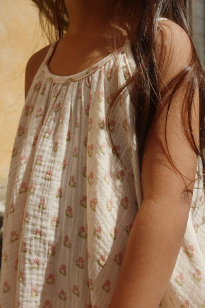 A child wearing the Konges Slojd Girls’ Coco Strap Dress stands outdoors, with long brown hair draped over one shoulder.