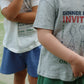 Two children stand outdoors on a green surface, both wearing Konges Slojd Baby Boys’ and Boys’ Spotty Sweat Shorts with an elastic waistband and t-shirts. One child has their arm across their chest while the other’s arms rest by their sides, with faces not visible.