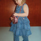 A toddler wearing a ruffled denim dress and matching Girls’ Elba Sparkle Jeans, holding a small pink circular bag.