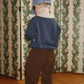 A child seen from behind, wearing a blue-striped cap, a blue long-sleeved shirt, and Konges Slojd Baby Boys’ and Boys’ Remy Pants in brown.