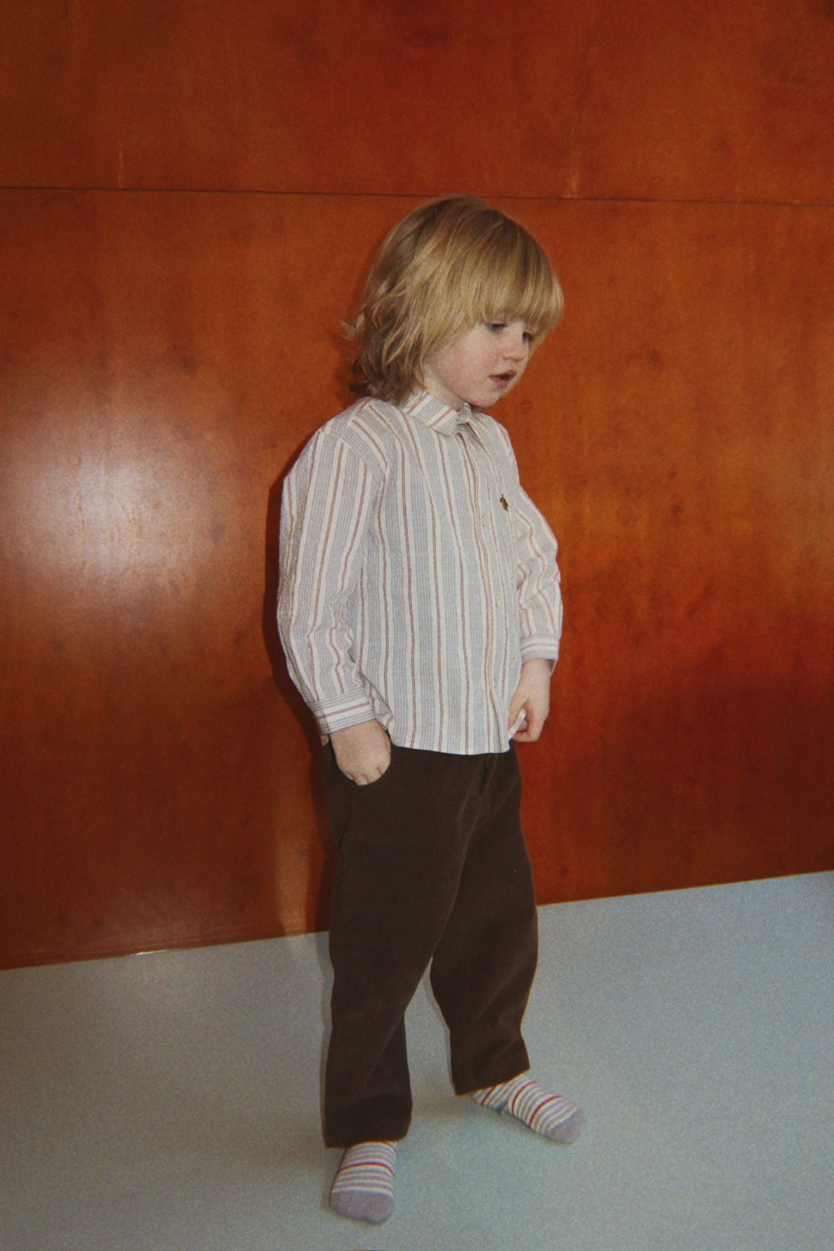 A young child wears a striped button-down shirt and relaxed-fit Baby Boys’ and Boys’ Remy Pants by Konges Slojd.
