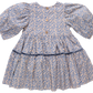 The Girls' Maribelle Dress by Pink Chicken showcases a blue climbing floral print on cotton poplin, puff sleeves, three wooden back buttons, and a gathered skirt with a dark blue ribbon at the waist.