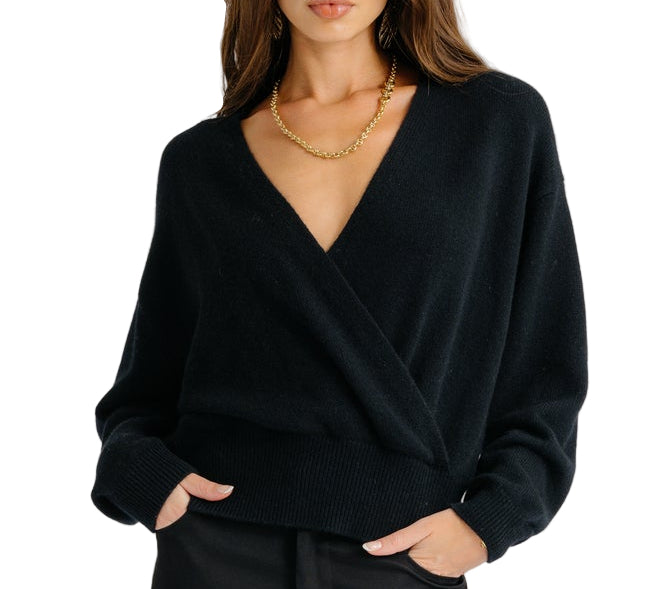 Model wearing the Sablyn Koda Wrap Cashmere Sweater in black—featuring a deep V neckline—paired with black pants and a gold necklace, shown from mid-thigh up against a white background.