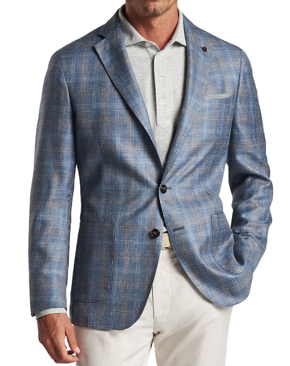 A man wearing the Peter Millar Andover Plaid Soft Jacket, a blue blazer crafted from a lightweight wool blend, over a light gray button-up shirt and white pants, with his left hand in his pocket.