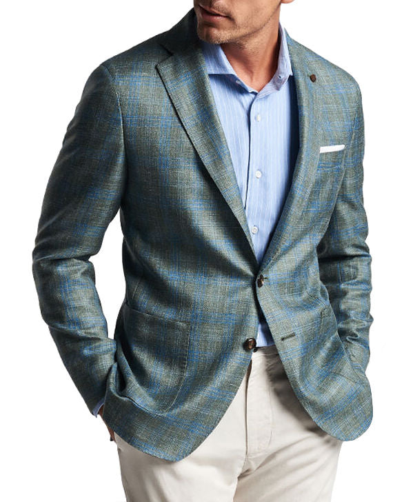 A person in a light blue shirt, Peter Millar Tremont Plaid Soft Jacket made of Italian wool, and beige pants stands with hands in their pockets. The head is partially cropped out of the frame.