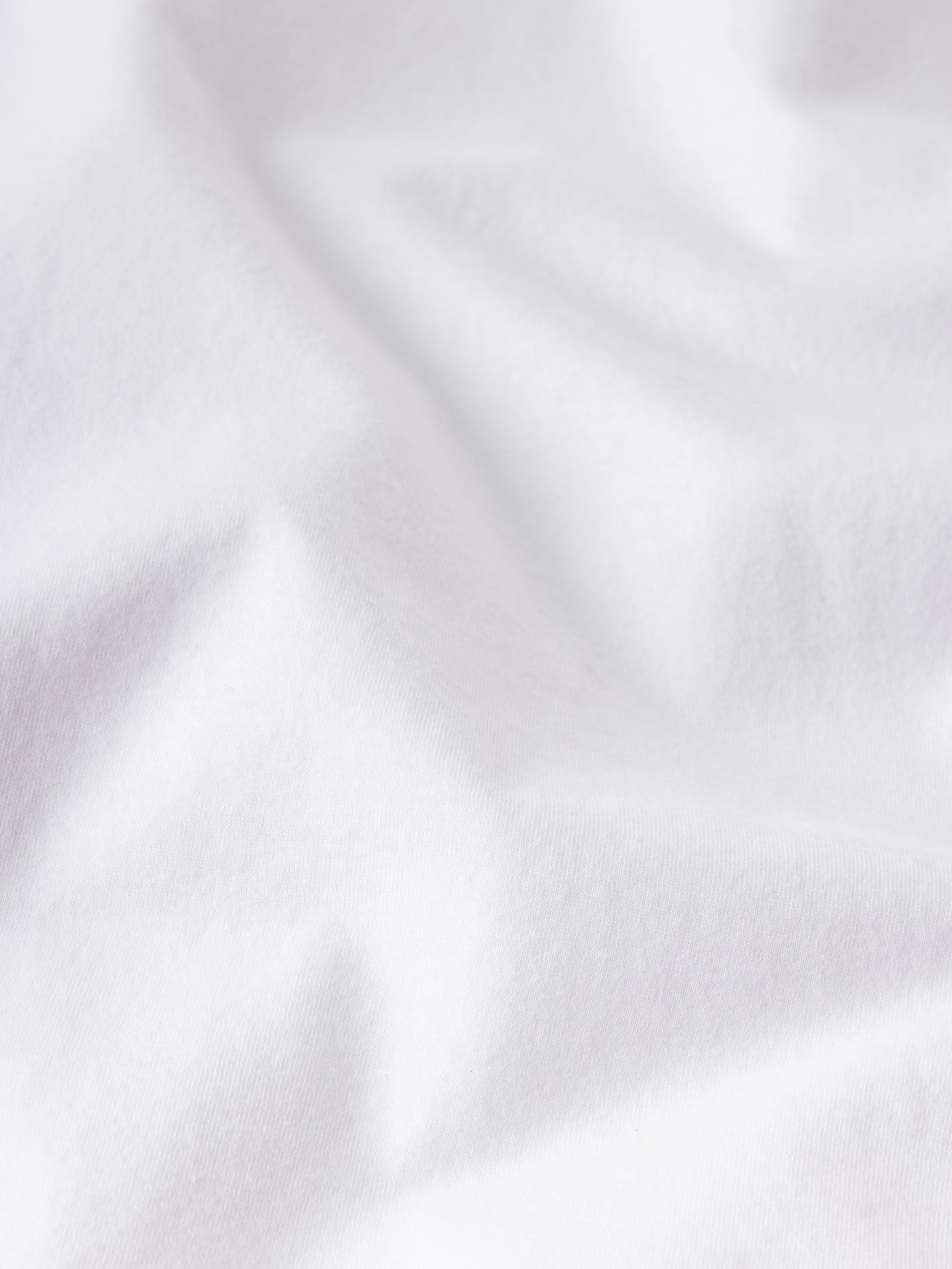 Close-up of white Supima cotton fabric with soft folds and gentle shadows, highlighting the luxurious feel of the Frame Light Cotton Tee—perfect for lightweight comfort and everyday style.