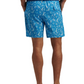 A person wearing a navy shirt, Peter Millar Saltwater Spirits Swim Trunk featuring an exclusive hand-designed print, and gray sneakers is shown from the back.