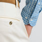 Close-up of a person wearing Peter Millar Signature Sateen Flat Front Trousers in cream, styled with a blue plaid shirt and tan belt. Features comfort waistband for an easy fit all day, highlighting the shirt cuff and back pocket.