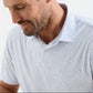 A bearded man looks down with a slight smile, wearing the Peter Millar Featherweight Land Of The Free Performance Polo, a lightweight patterned shirt with UPF 50+ sun protection, photographed from the shoulders up.