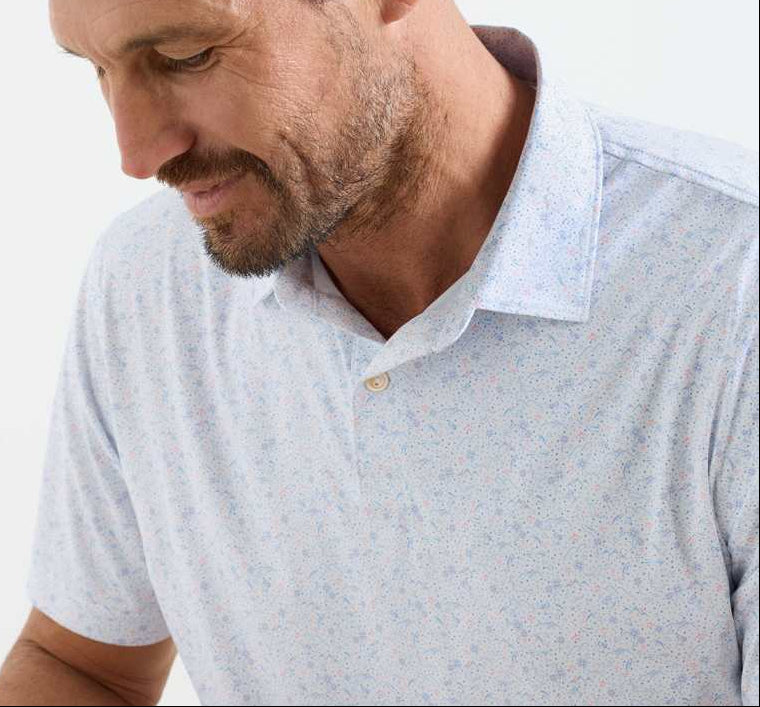 A bearded man looks down with a slight smile, wearing the Peter Millar Featherweight Land Of The Free Performance Polo, a lightweight patterned shirt with UPF 50+ sun protection, photographed from the shoulders up.