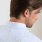 A man with brown hair is seen from behind and slightly to the side, wearing a white Peter Millar Nice Shot Performance Jersey Polo with a blue and pink abstract pattern.