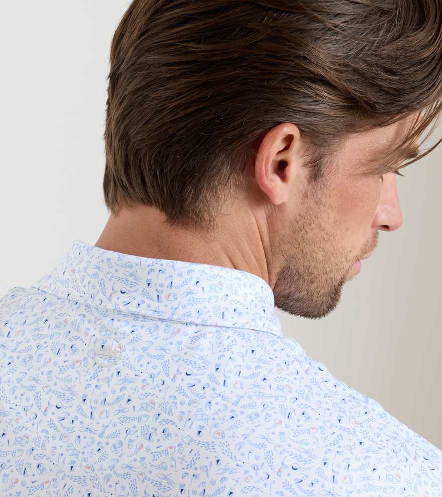 A man with brown hair is seen from behind and slightly to the side, wearing a white Peter Millar Nice Shot Performance Jersey Polo with a blue and pink abstract pattern.