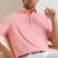 A man sits on a light chair wearing the Peter Millar Merion Performance Jersey Polo in pink and white stripes with UPF 50+ protection and light pants.