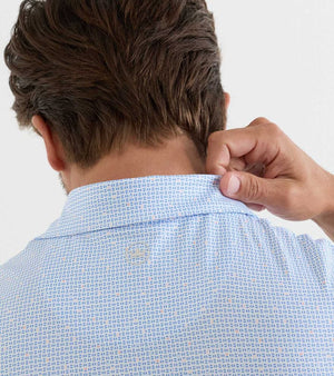 A person seen from behind lifts the collar of a Peter Millar Alta Performance Jersey Polo in light blue pattern with their right hand, highlighting its four-way stretch material.
