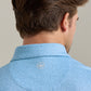 A man is shown from behind wearing the Peter Millar Magnolia Performance Jersey Polo in light blue with a pattern, four-way stretch, and a small white embroidered logo at the neck.