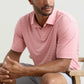 A man seated on a chair wears the Peter Millar Featherweight Stripe Performance Polo in light pink and white, paired with light gray shorts.
