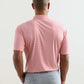A person stands with their back to the camera, wearing the Peter Millar Featherweight Stripe Performance Polo in light pink, featuring UPF 50+ protection and four-way stretch, paired with light gray pants against a plain background.