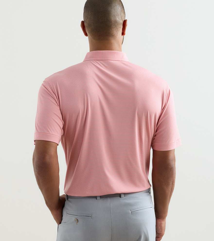 A person stands with their back to the camera, wearing the Peter Millar Featherweight Stripe Performance Polo in light pink, featuring UPF 50+ protection and four-way stretch, paired with light gray pants against a plain background.