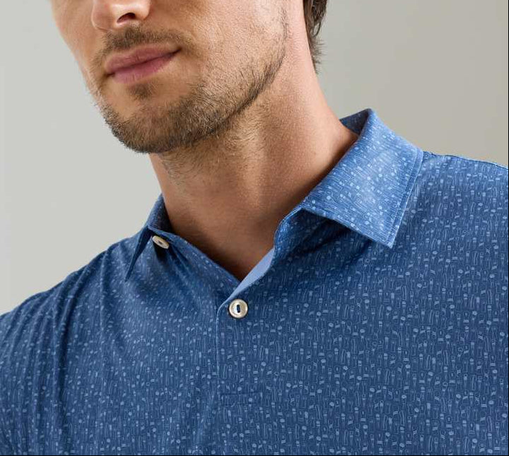 A man wearing the Peter Millar Featherweight Headcovers Performance Polo, a blue patterned, lightweight shirt with white buttons and UPF 50+ sun protection, shown from the chest up.