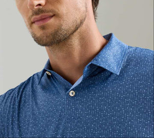 A man wearing the Peter Millar Featherweight Headcovers Performance Polo, a blue patterned, lightweight shirt with white buttons and UPF 50+ sun protection, shown from the chest up.