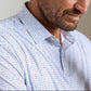A man wears the Peter Millar Featherweight Cornhole Performance Polo—a light button-up with a multicolored geometric print and four-way stretch, shown from the shoulders up for a polished, all-day comfortable look.