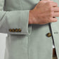 A person is shown from the chest down adjusting the front of a light green, garment-dyed Weekend Soft Jacket by Peter Millar, featuring brown buttons.