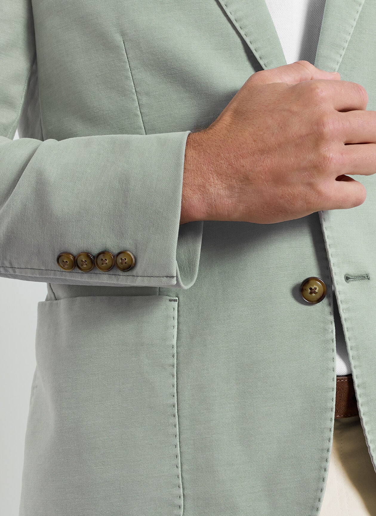 A person is shown from the chest down adjusting the front of a light green, garment-dyed Weekend Soft Jacket by Peter Millar, featuring brown buttons.