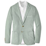 The Weekend Soft Jacket by Peter Millar is a light green, garment-dyed unstructured blazer with notch lapels, two brown buttons, and patch pockets, paired with a white dress shirt.