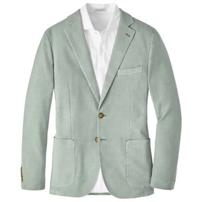 The Weekend Soft Jacket by Peter Millar is a light green, garment-dyed unstructured blazer with notch lapels, two brown buttons, and patch pockets, paired with a white dress shirt.