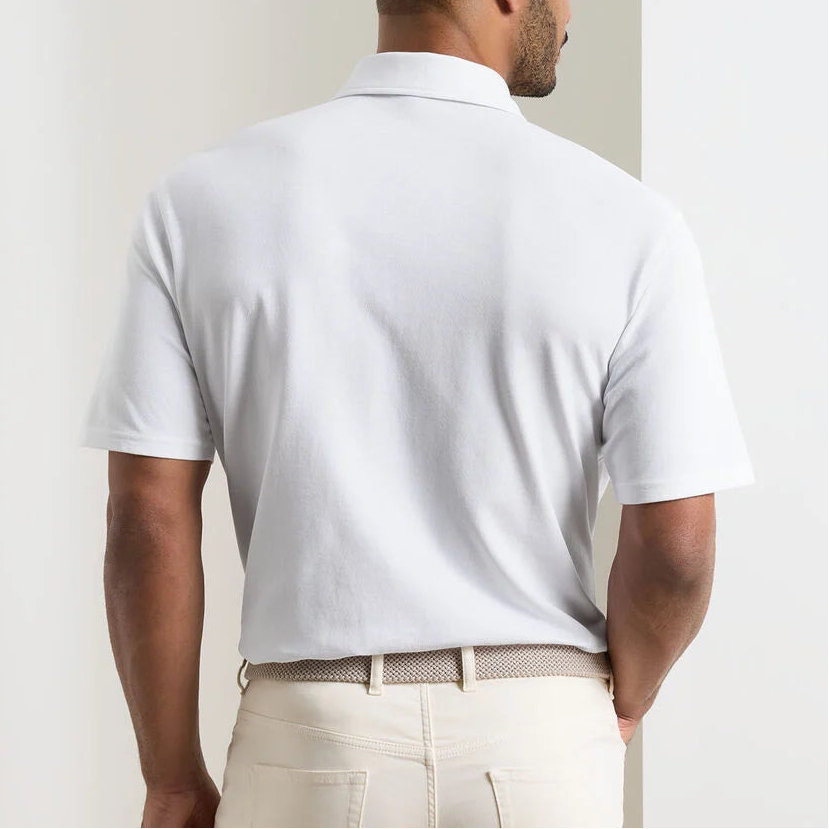 A man stands with his back to the camera wearing the Peter Millar Everyday Pique Polo and light-colored trousers in front of a white wall.