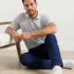 A man in a light gray Peter Millar Gilman Crown Flex Cotton Polo and navy pants sits on the floor beside a chair, looking at the camera.