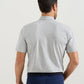 A man faces away from the camera wearing a Peter Millar Gilman Crown Flex Cotton Polo in light gray with a cutaway collar and dark blue pants, perfect for casual wear against a plain background.