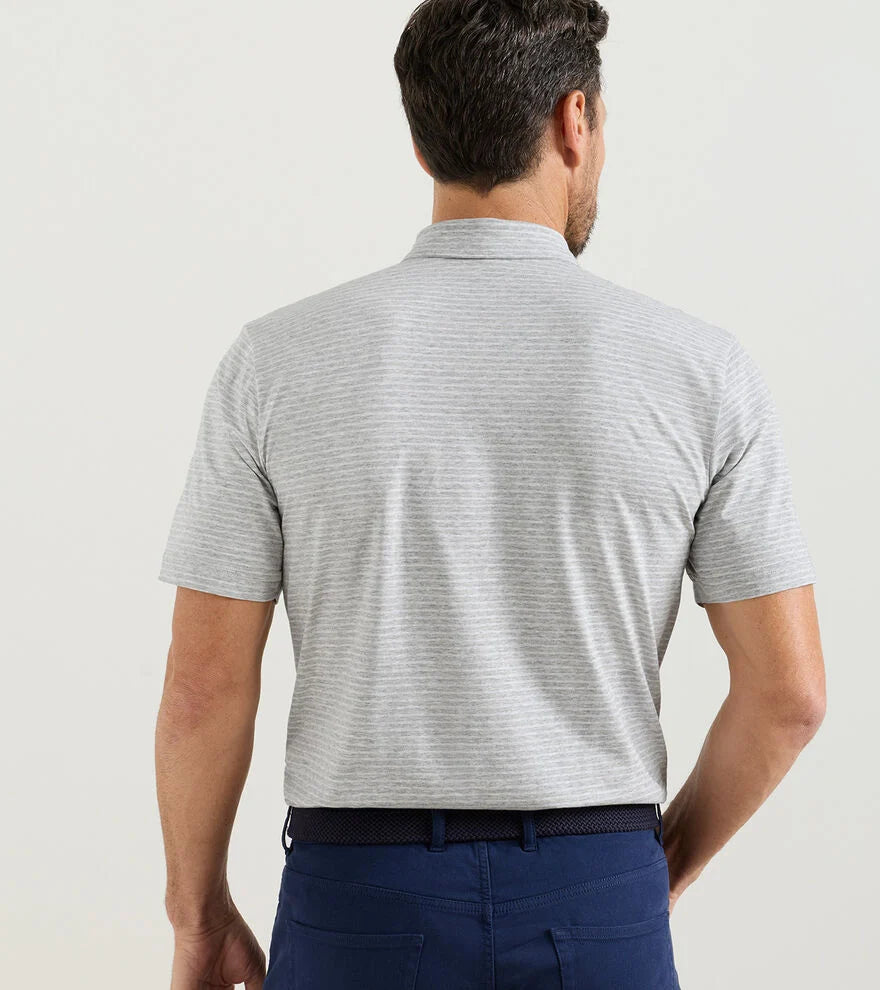 A man faces away from the camera wearing a Peter Millar Gilman Crown Flex Cotton Polo in light gray with a cutaway collar and dark blue pants, perfect for casual wear against a plain background.