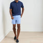 A man stands indoors wearing a navy polo, Peter Millar Nautical Ropes Swim Trunk with elastic waistband and mesh liner, and black slip-on shoes against a plain white wall and light wood floor.