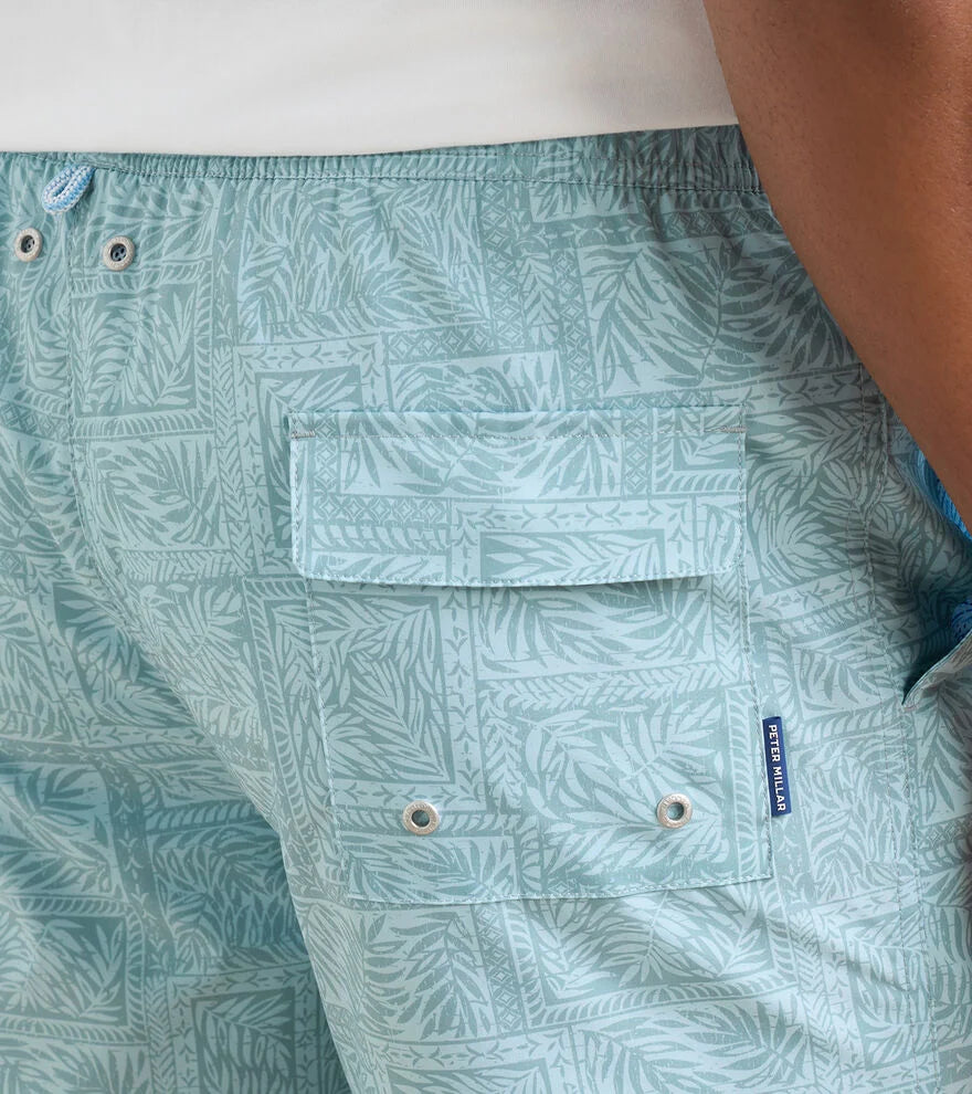 Close-up of a person wearing Peter Millar Seaside Shade Swim Trunk featuring an elastic waistband, flap pocket, metal grommets, and quick-drying light blue patterned fabric.