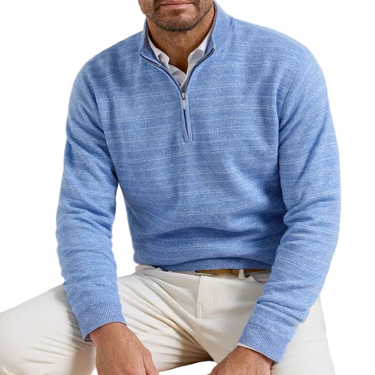 A man wears the Peter Millar Saratoga Striped Quarter-Zip Sweater over a collared shirt and white pants, seated with his upper body visible against a white background.