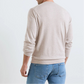 A person wearing the Peter Millar Lake Long Sleeve Sweater in light beige with blue jeans stands facing away from the camera against a plain background.