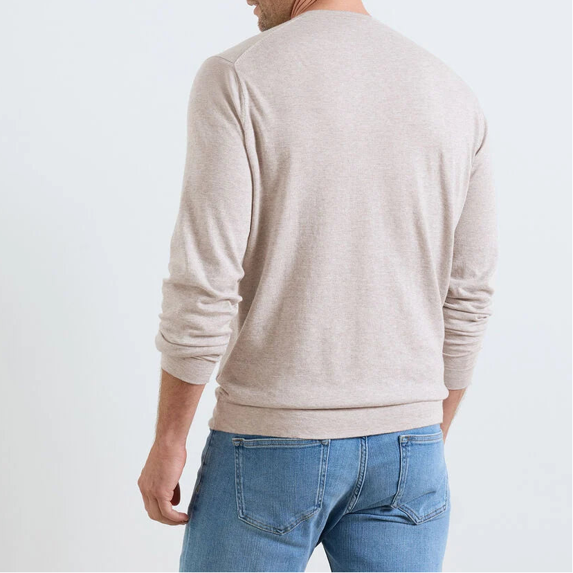 A person wearing the Peter Millar Lake Long Sleeve Sweater in light beige with blue jeans stands facing away from the camera against a plain background.