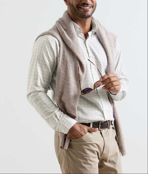 A man in a Peter Millar Douglas Crown Lite Cotton-Stretch Sport Shirt, beige stretch cotton pants, and a sweater over his shoulders holds sunglasses in his right hand and smiles.